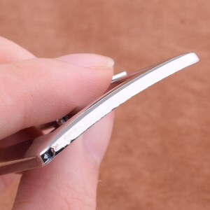 May include: Close-up of a silver metal belt buckle with a smooth, polished finish.