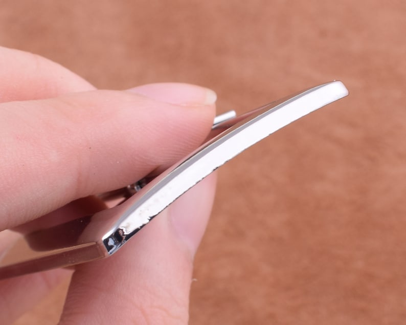 May include: Close-up of a silver metal belt buckle with a smooth, polished finish.