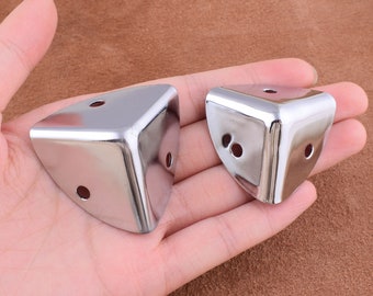 May include: Two silver corner protectors with three holes each. The protectors are designed to protect furniture corners from damage.