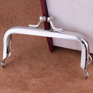 May include: Silver-toned metal purse frame with two round decorative knobs at the top.