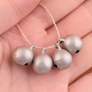 May include: Five silver jingle bells strung together on a white cord. The bells are round and have a smooth, shiny finish.