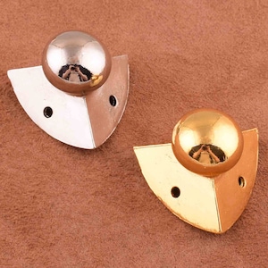 May include: Two metal corner protectors with a rounded, shiny finish. One is gold and the other is silver.