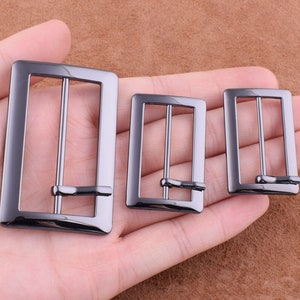 May include: Three black metal belt buckles of different sizes. The buckles are rectangular with a smooth finish.