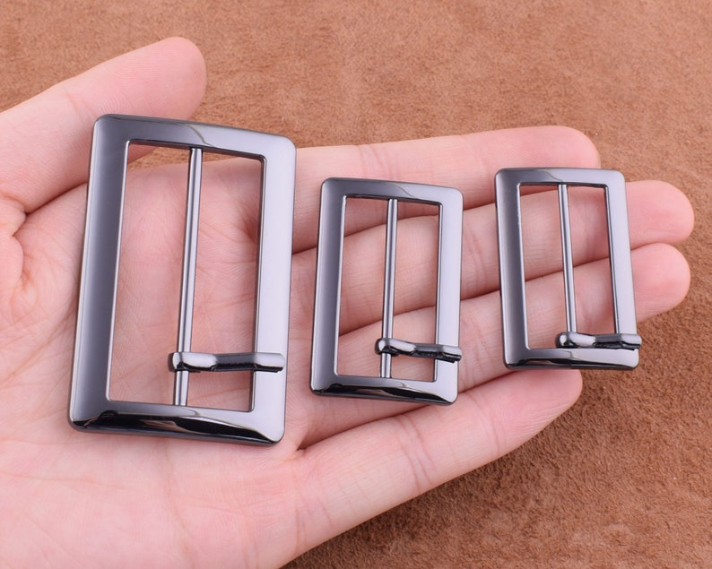 May include: Three black metal belt buckles of different sizes. The buckles are rectangular with a smooth finish.
