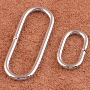 May include: Two silver metal oval rings, one larger than the other, on a brown leather background.