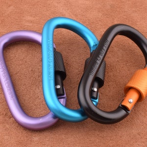 Peut inclure: Trois mousquetons métalliques de couleurs différentes : bleu, violet et noir. Le mousqueton bleu porte la mention "NOT FOR CLIMBING" gravée. Le mousqueton noir porte la mention "SWIVEL TO 360 DEG" gravée.