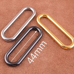May include: Three oval-shaped metal rings in silver, black, and gold. The black ring has a measurement of 44mm.