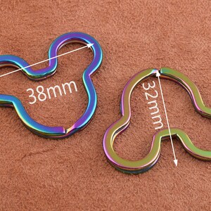 K&ouml;nnte beinhalten: Zwei regenbogenfarbene Schl&uuml;sselanh&auml;nger aus Metall in Form von Mickey-Maus-Ohren. Der gr&ouml;&szlig;ere Schl&uuml;sselanh&auml;nger misst 38 mm und der kleinere 32 mm.