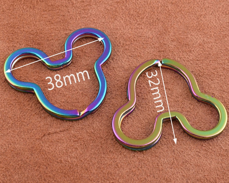K&ouml;nnte beinhalten: Zwei regenbogenfarbene Schl&uuml;sselanh&auml;nger aus Metall in Form von Mickey-Maus-Ohren. Der gr&ouml;&szlig;ere Schl&uuml;sselanh&auml;nger misst 38 mm und der kleinere 32 mm.