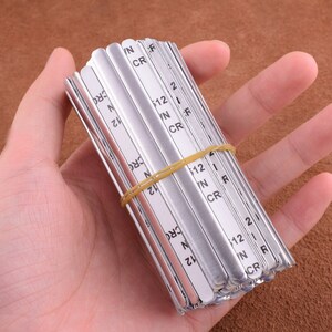 May include: A stack of silver metal nose wire for face masks. The wires are labeled with the letters "N", "IN", "CR", "F", and "R" and the numbers "12" and "2".