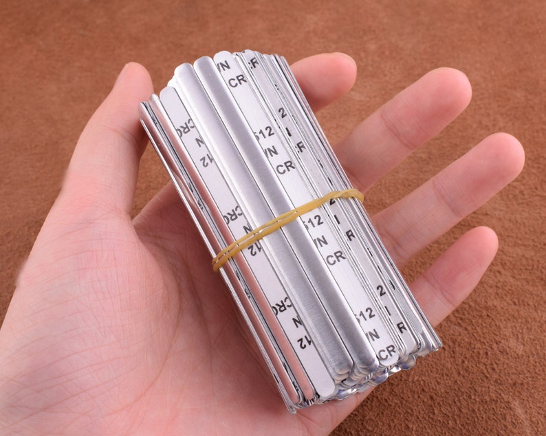 May include: A stack of silver metal nose wire for face masks. The wires are labeled with the letters "N", "IN", "CR", "F", and "R" and the numbers "12" and "2".