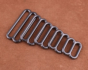 Op de afbeelding: Een set van acht zwarte metalen D-ringen in verschillende maten. De ringen zijn in een driehoekige vorm gerangschikt, met de grootste ring bovenaan en de kleinste ring onderaan.