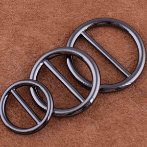 May include: Three black metal rings with a center bar. The rings are different sizes and are arranged in a row.