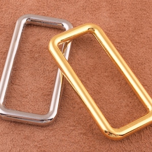 May include: Two metal belt loops, one silver and one gold, on a brown suede background.