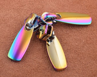 May include: Three iridescent zipper pulls in a rainbow color scheme. The pulls are made of metal and have a smooth, shiny finish.