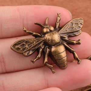 May include: A bronze bee charm with detailed wings and a textured body. The bee is a popular motif in jewelry and crafts.