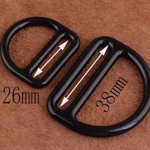 Peut inclure: Deux anneaux en D en m&eacute;tal noir avec une finition polie. Le plus grand anneau mesure 38 mm de diam&egrave;tre et le plus petit anneau mesure 26 mm de diam&egrave;tre.