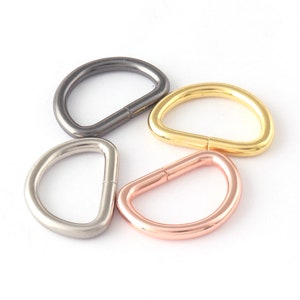 May include: Four metal D-rings in different finishes: black, silver, gold, and rose gold. These rings are commonly used for attaching straps, handles, or other accessories to bags, purses, or other items.