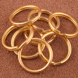 Könnte beinhalten: Sechs goldfarbene Schlüsselringe aus Metall, die auf einer braunen Oberfläche gestapelt sind.