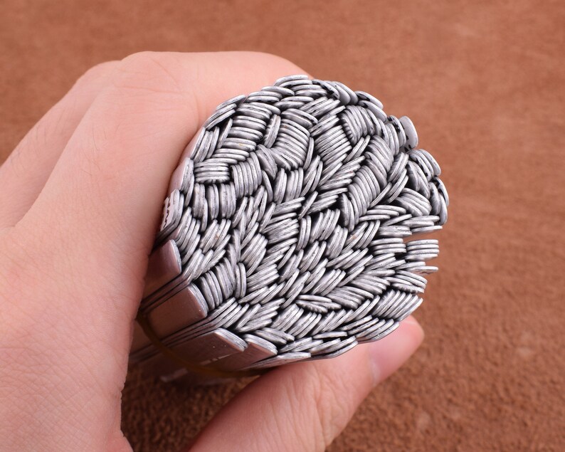 May include: A close-up of a stack of silver metal rings, woven together in a basket weave pattern.