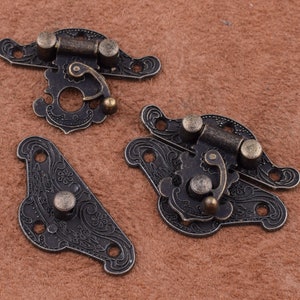 May include: Three antique-style metal clasps with ornate floral designs. The clasps are in a dark bronze color and have a hinged design with a small latch.