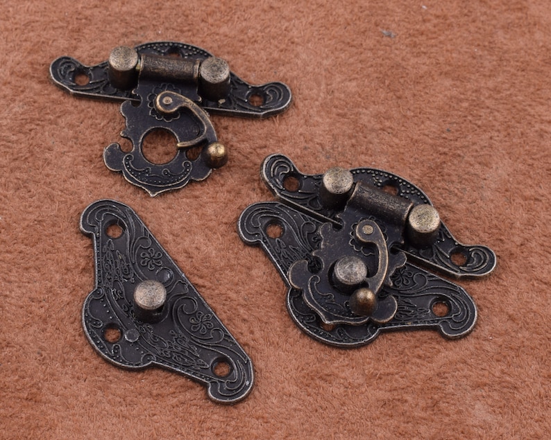 May include: Three antique-style metal clasps with ornate floral designs. The clasps are in a dark bronze color and have a hinged design with a small latch.