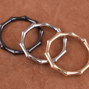 May include: Three metal rings with a bamboo-like design. The rings are black, silver, and gold.