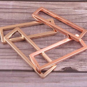 May include: Three rose gold metal belt buckle clasps. The clasps are rectangular and have a smooth, polished finish.