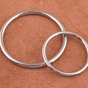 May include: Two silver metal rings, one larger than the other, are shown on a brown textured surface.