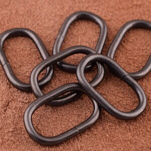 May include: Five black metal rings, each with a circular shape and a smooth finish. The rings are interlocked, creating a decorative and functional design.