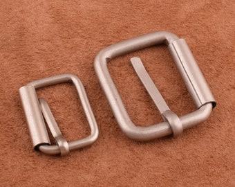 Op de afbeelding: Twee zilveren metalen riemgespen in verschillende maten. De grotere gesp is ongeveer 5 cm breed en de kleinere gesp is ongeveer 2,5 cm breed.