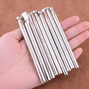 May include: A set of 10 silver leather craft tools with different sized tips. The tools are held in a hand.