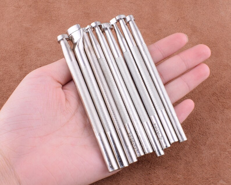 May include: A set of 10 silver leather craft tools with different sized tips. The tools are held in a hand.