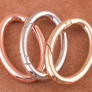 May include: Three metal key rings in different colours: rose gold, silver, and gold. The rings are linked together.