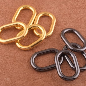May include: A collection of oval-shaped metal rings in gold and dark gray. The rings are arranged in small groups, with a focus on their smooth, polished surfaces. The background is a warm, neutral tone, highlighting the metallic sheen of the rings.