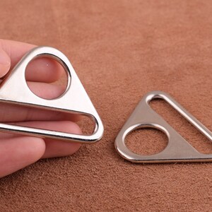 Op de afbeelding: Twee zilveren driehoekige metalen ringen met een ronde opening in het midden. De ringen zijn bedoeld om aan banden of andere materialen te worden bevestigd.