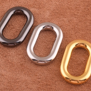 May include: Three oval-shaped metal rings in black, silver, and gold. The rings are on a brown suede surface.