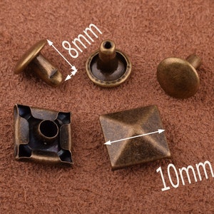 May include: Assortment of four antique gold metal rivets. Two are round with a protruding post, one is square with a raised pyramid shape, and one is square with a recessed center. The rivets measure 8mm and 10mm.