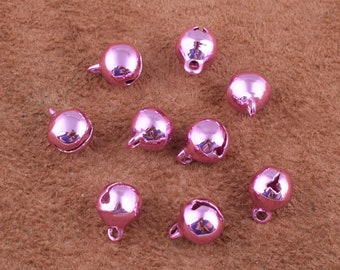 May include: A collection of ten pink metal jingle bells. The bells are round and have a small hole at the top for attaching to a string or other object.