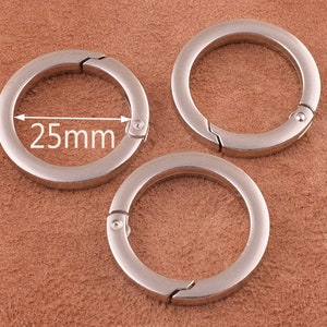 Puede incluir: Tres llaveros de metal plateado con un mecanismo de apertura de resorte. El llavero de la izquierda tiene una medida de 25 mm.