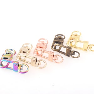 Peut inclure: Cinq fermoirs pivotants en métal de différentes couleurs : arc-en-ciel, or rose, or, bronze et argent. Chaque fermoir est doté d’un loquet à ressort et d’un anneau en D.