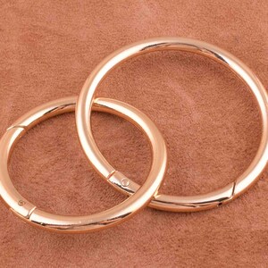May include: Two gold-toned metal key rings, one slightly larger than the other, are linked together. The rings are smooth and shiny.