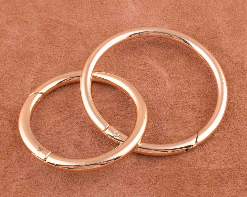 May include: Two gold-toned metal key rings, one slightly larger than the other, are linked together. The rings are smooth and shiny.