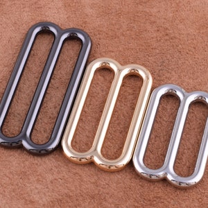 Puede incluir: Tres hebillas deslizantes de metal en diferentes acabados: negro, dorado y plateado. Cada hebilla tiene dos bucles paralelos.
