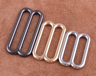 May include: Three metal slider buckles in different finishes: black, gold, and silver. Each buckle has two parallel loops.
