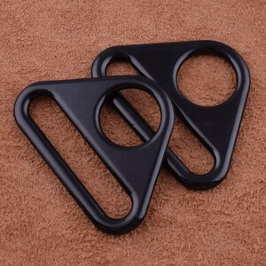 May include: Two black metal D-rings, shaped like triangles, with a smooth finish. The rings are interlocked.