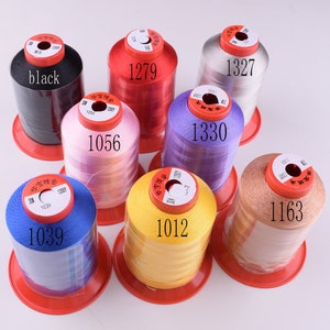 May include: A collection of ten spools of thread in various colors, including black, red, pink, purple, beige, yellow, and silver. Each spool has a label with a number printed on it, such as 1039, 1056, 1279, 1327, 1330, 1163, and 1012.