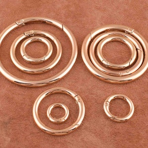 May include: Five gold-toned metal key rings of varying sizes. The key rings are all circular and have a spring-loaded opening mechanism.