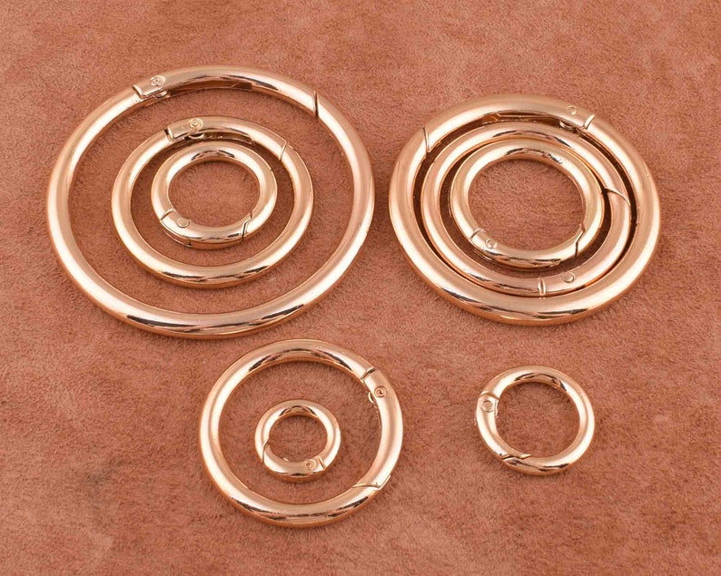May include: Five gold-toned metal key rings of varying sizes. The key rings are all circular and have a spring-loaded opening mechanism.