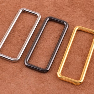 May include: Three metal belt loops in silver, black, and gold. The loops are rectangular with rounded corners.